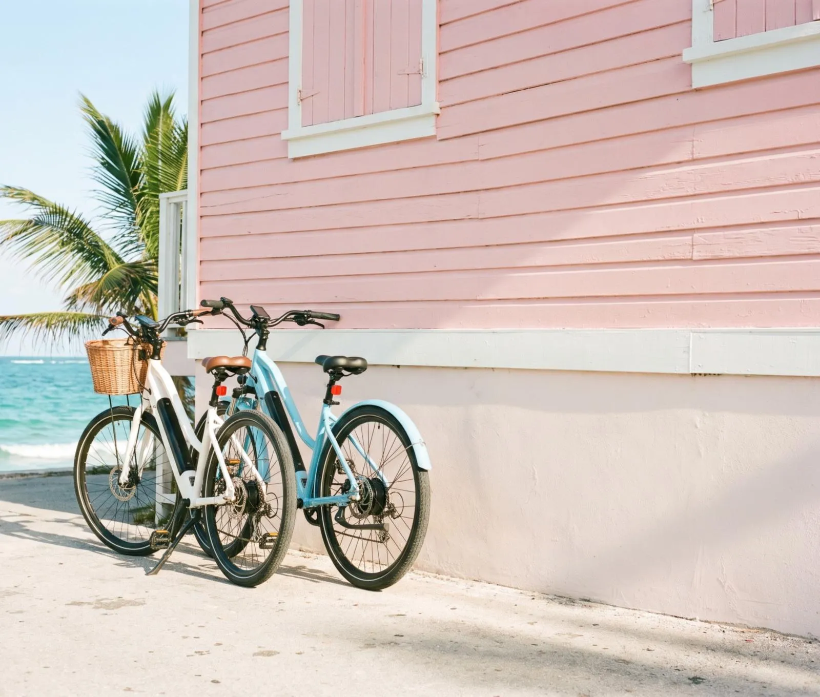 Two e-bikes leaning on a pastel wall by the sea